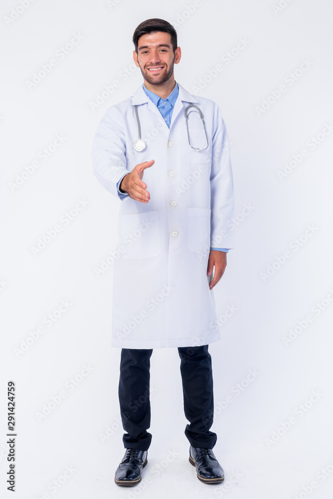 Full body shot of happy young bearded Persian man doctor giving handshake Full body shot of happy young bearded Persian man doctor giving handshake