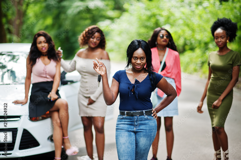 Group of five happy african american girls posed against car, one of them show keys. Group of five happy african american girls posed against car, one of them show keys.