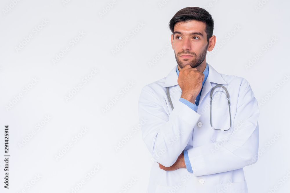Portrait of young bearded Persian man doctor thinking and looking up Portrait of young bearded Persian man doctor thinking and looking up
