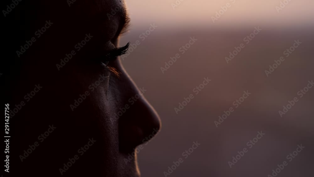 Woman thinking and looking out from train window, extreme close up shot of her eye. Blurred background, dim natural light at evening time. High speed carriage run fast, slow motion shot