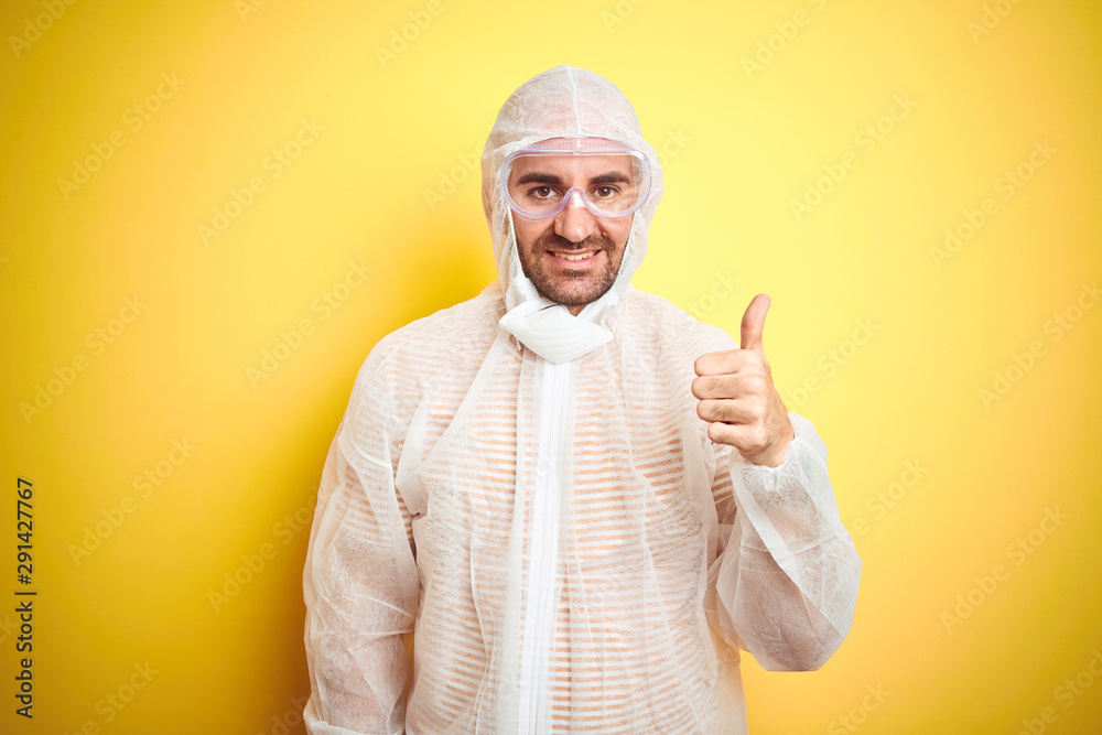Naklejka premium Young man wearing painter equipment and safety glasses over isolated yellow background happy with big smile doing ok sign, thumb up with fingers, excellent sign