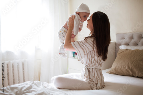 happy smiling young mother playing with her with newborn baby in the bedroom. parenthood concept
