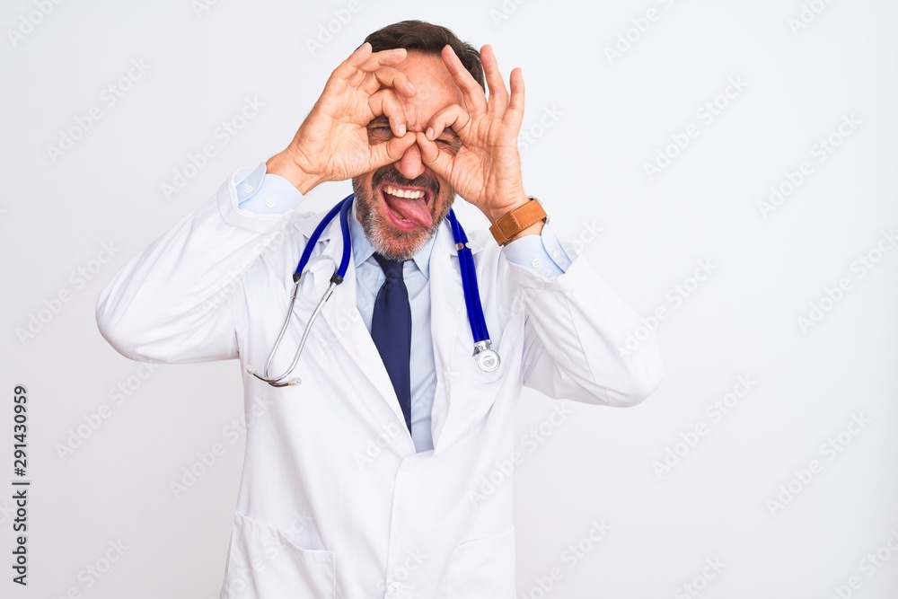 Middle age doctor man wearing coat and stethoscope standing over isolated white background doing ok gesture like binoculars sticking tongue out, eyes looking through fingers. Crazy expression. Middle age doctor man wearing coat and stethoscope standing over isolated white background doing ok gesture like binoculars sticking tongue out, eyes looking through fingers. Crazy expression.