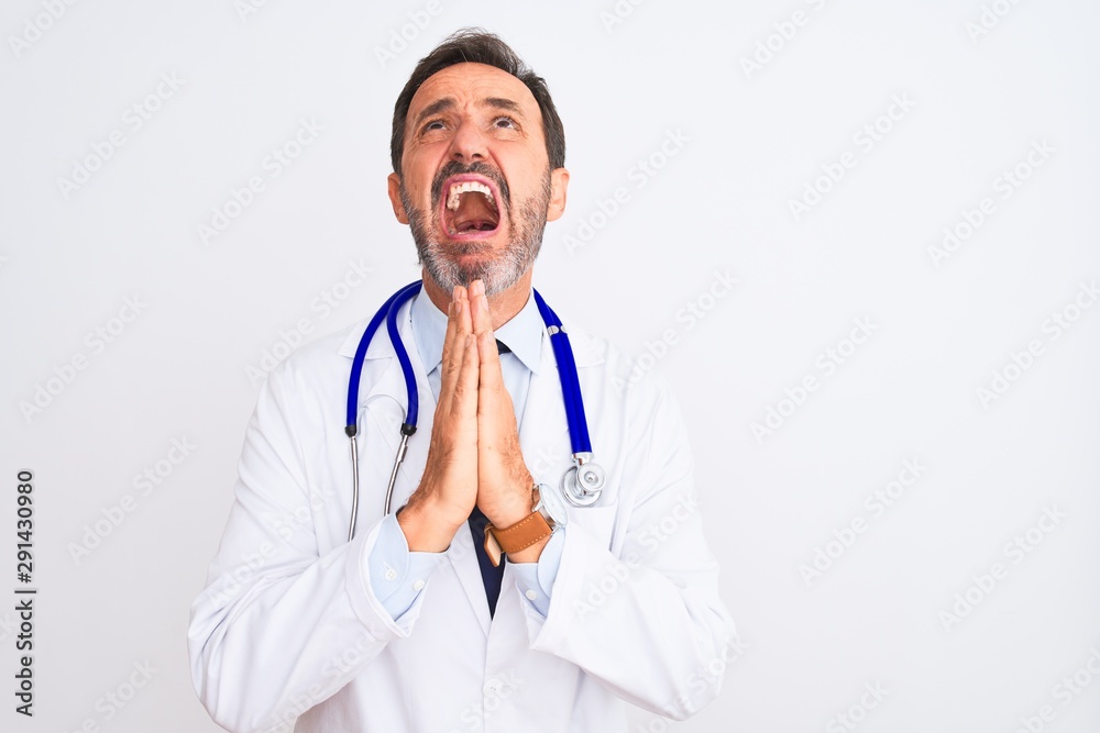 Middle age doctor man wearing coat and stethoscope standing over isolated white background begging and praying with hands together with hope expression on face very emotional and worried Middle age doctor man wearing coat and stethoscope standing over isolated white background begging and praying with hands together with hope expression on face very emotional and worried