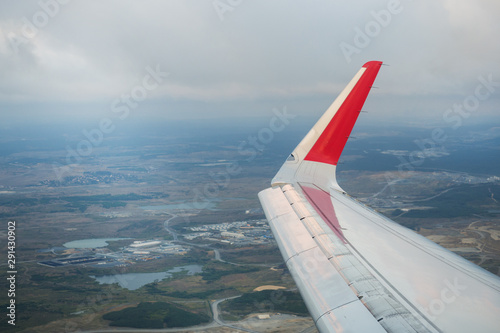 View the wing of the passenger plane and the ground from the window of the flying aircraft.