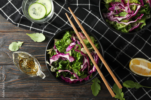 Black bowls with salad, chopsticks and towel on wooden background, top view
