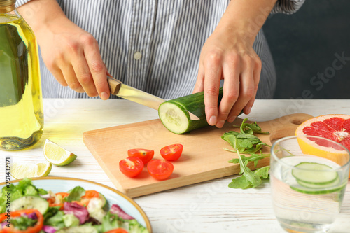 Young woman slices cucumber for salad on wooden background