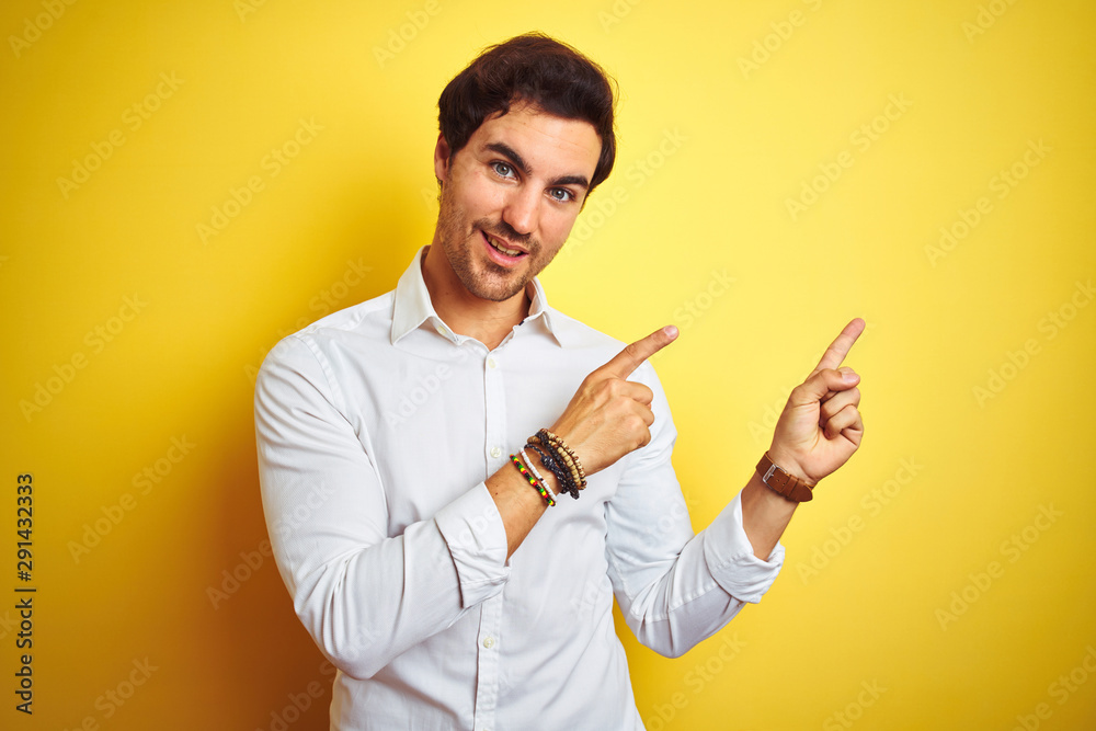 Young handsome businessman wearing elegant shirt standing over isolated yellow background smiling and looking at the camera pointing with two hands and fingers to the side. Young handsome businessman wearing elegant shirt standing over isolated yellow background smiling and looking at the camera pointing with two hands and fingers to the side.