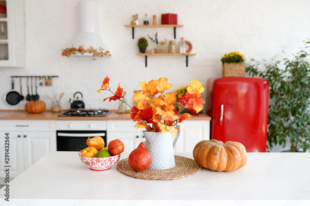 autumn table with vegetables in kitchen. red and yellow leaves in the vase and pumpkin on white background. autumn table with vegetables in kitchen. red and yellow leaves in the vase and pumpkin on white background.