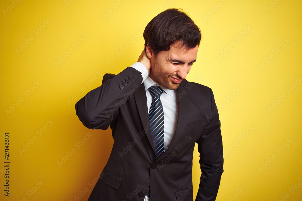 Young handsome businessman wearing suit and tie standing over isolated yellow background Suffering of neck ache injury, touching neck with hand, muscular pain Young handsome businessman wearing suit and tie standing over isolated yellow background Suffering of neck ache injury, touching neck with hand, muscular pain