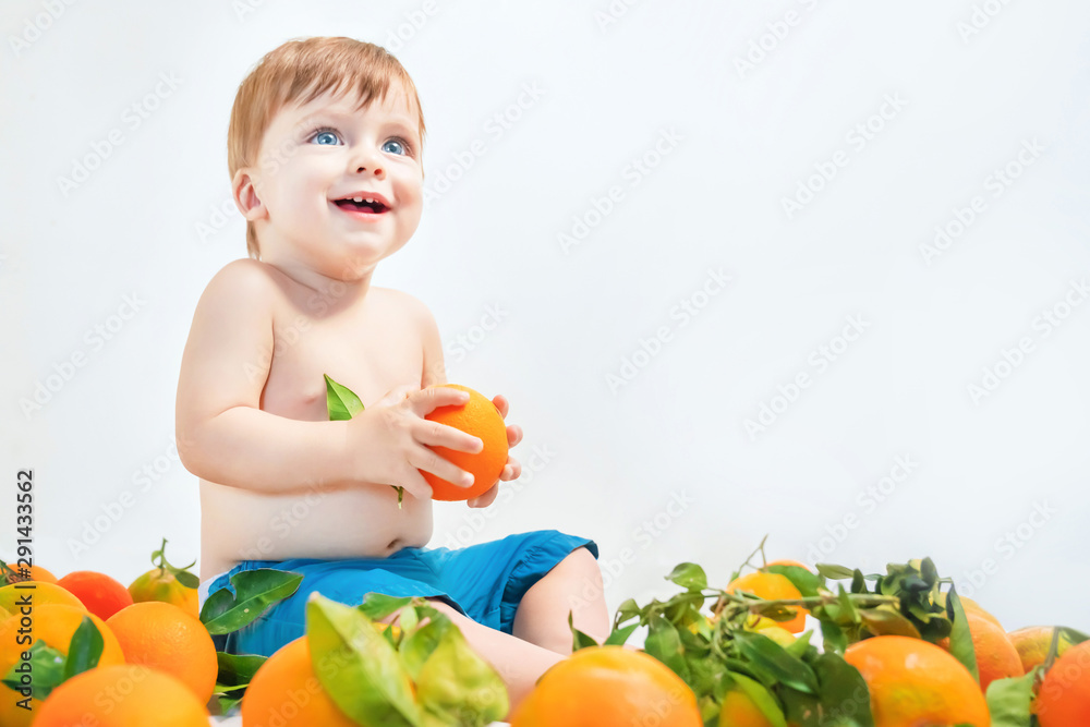 Laughing blue-eyed baby sits in oranges on a light background. Laughing blue-eyed baby sits in oranges on a light background.