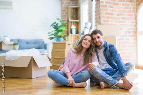 Young beautiful couple moving to a new house sitting on the floor with serious expression on face. Simple and natural looking at the camera.