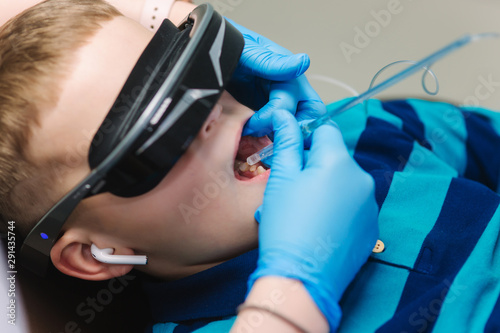 Close up of little boy sitting in dentist in vr glasses and wireless headphones while dentist make x-ray of teeth