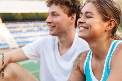 Image of joyful man and woman smiling while sitting on tennis court © Drobot Dean