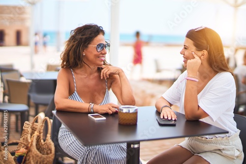 Beautiful mother and daugther sitting at terrace of a restaurant speaking and smiling