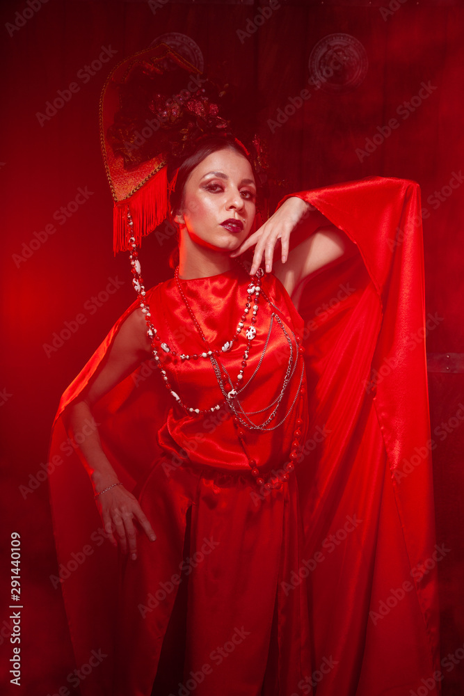 strict stylish girl in a fashionable long red dress and a voluminous hat on the background of smoke in the Studio at night alone. Halloween concept. strict stylish girl in a fashionable long red dress and a voluminous hat on the background of smoke in the Studio at night alone. Halloween concept.