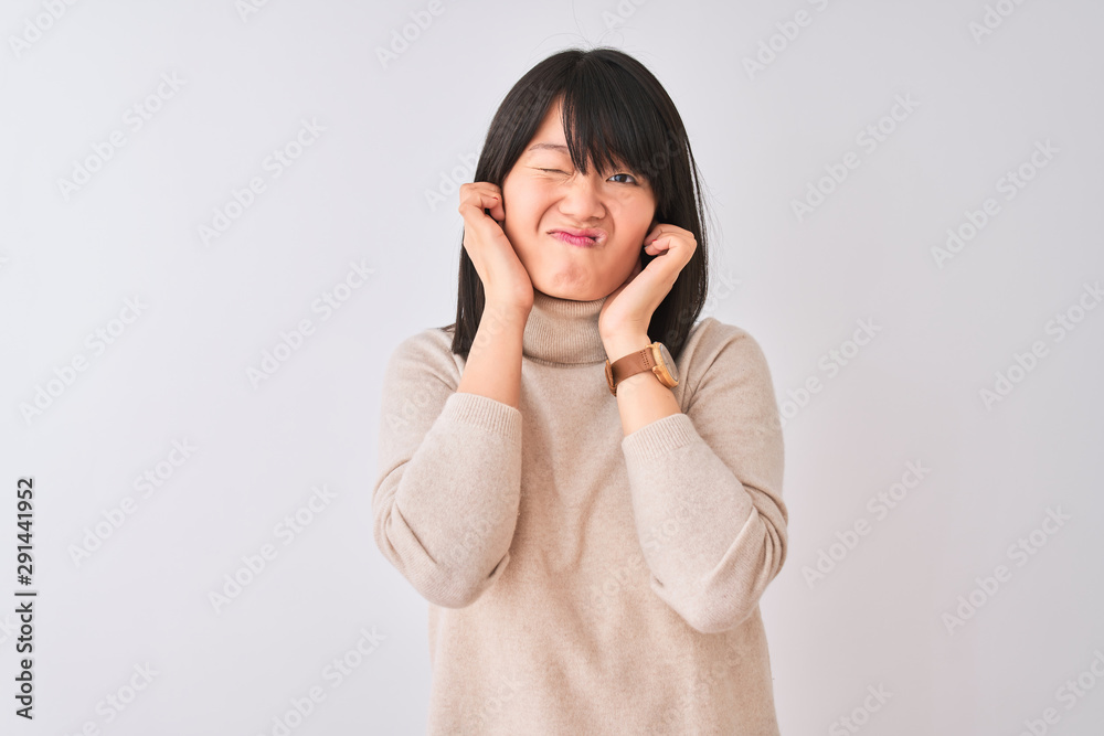 Young beautiful chinese woman wearing turtleneck sweater over isolated white background covering ears with fingers with annoyed expression for the noise of loud music. Deaf concept. Young beautiful chinese woman wearing turtleneck sweater over isolated white background covering ears with fingers with annoyed expression for the noise of loud music. Deaf concept.