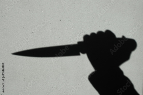 Knife in a hand shadow on a gray wall