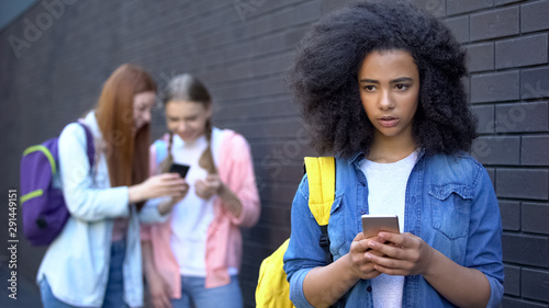 Sad african schoolgirl reading humiliating message, cyber bullying embarrassment photo