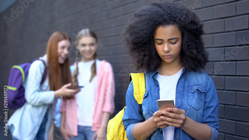 Upset black student smartphone, laughing classmates standing behind, bullying photo