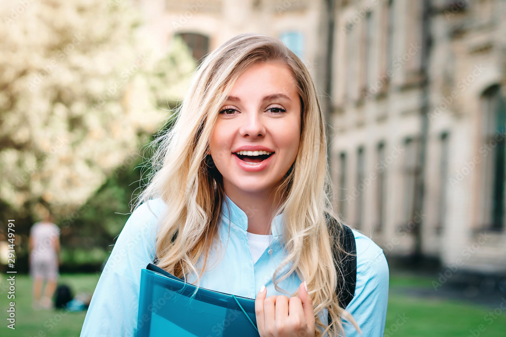 A blonde student girl is laughing and holding a folder and a notebook ...