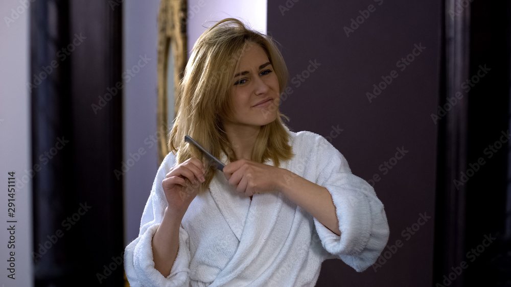Dissatisfied girl hardly combing dry hair in front of mirror, beauty problem Dissatisfied girl hardly combing dry hair in front of mirror, beauty problem
