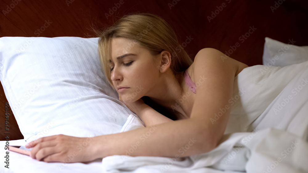 Female looking at cellphone sleeping in bed, dont want to wake up morning alarm Female looking at cellphone sleeping in bed, dont want to wake up morning alarm