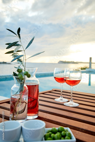 two glasses of rose wine with  olives against blue water on a pier..