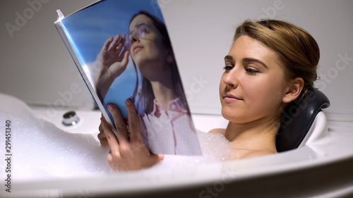 Beautiful woman reading magazine in bath with foam bubbles, evening relax