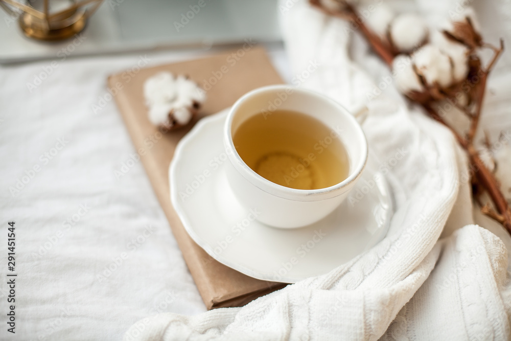 White mug with tea, cotton, laptop, plaid on the bed. Breakfast in bed. Cozy. Autumn. Winter. White mug with tea, cotton, laptop, plaid on the bed. Breakfast in bed. Cozy. Autumn. Winter.