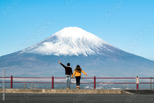A happy Asian couple hold hand each other looking at big dramatic view of famous mount Fuji in early winter from the hill . Concept of Japan travel with copy space on top. © 9mot