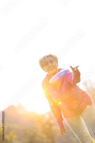 Active senior woman throwing disc in park with yellow lens flare in background