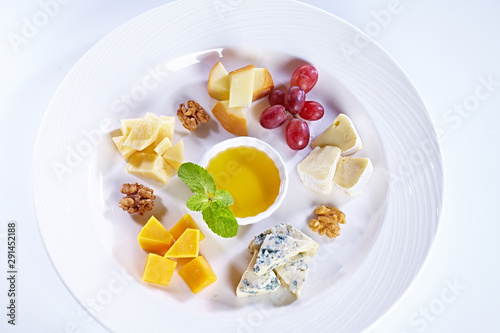 Different type of cheese with honey  grape  nuts on white plate. Top view. Blue cheese  cheddar  parmesan  maasdam and brie cheese slices