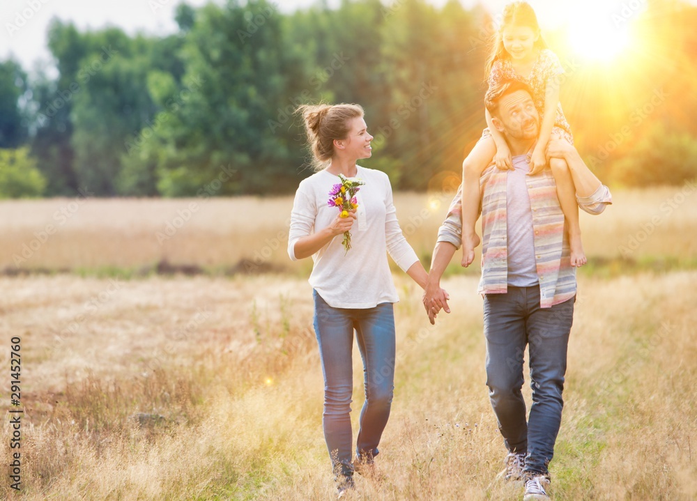 Fototapeta premium Father carrying his daughter on shoulders while walking with his wife in field