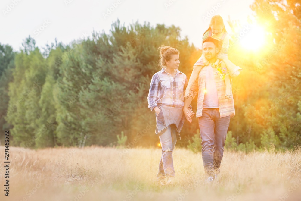 Father carrying his daughter on shoulders while walking with his wife in field