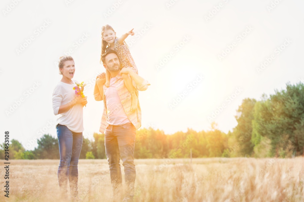 Fototapeta premium Happy family walking in wheat field with yellow lens flare in background