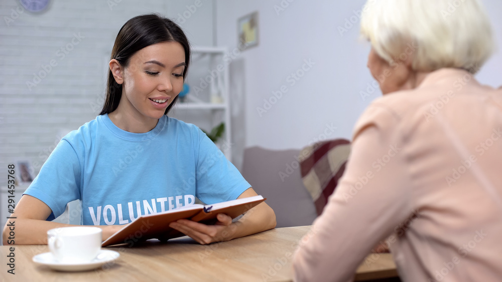 Smiling social worker reading book senior retired lady, generations togetherness Smiling social worker reading book senior retired lady, generations togetherness