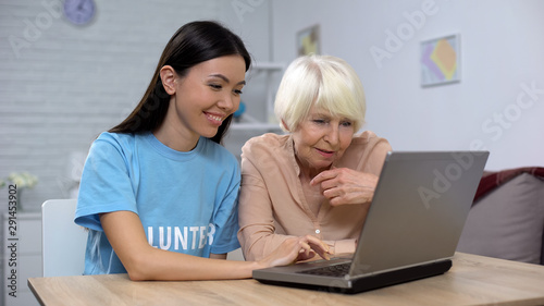 Nursing home volunteer teaching aged lady to use laptop, online app, technology