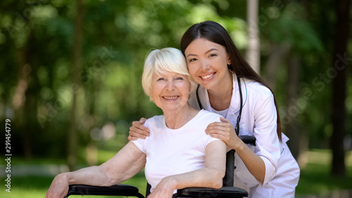 Smiling female nurse hugging disabled elderly woman and looking at camera