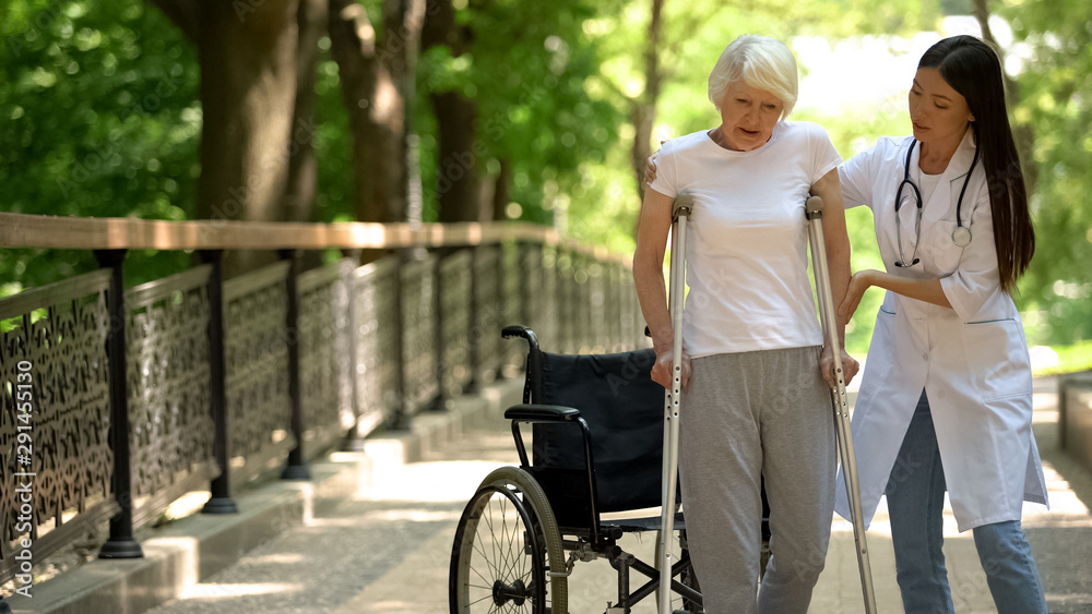 Doctor helping disabled old woman walking with crutches, recovery after trauma Doctor helping disabled old woman walking with crutches, recovery after trauma