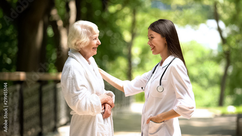 Smiling nurse talking with elderly woman in bathrobe at sanatoria park, relax © motortion