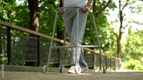 Legs of patient moving with help of walking frame in hospital park, rehab