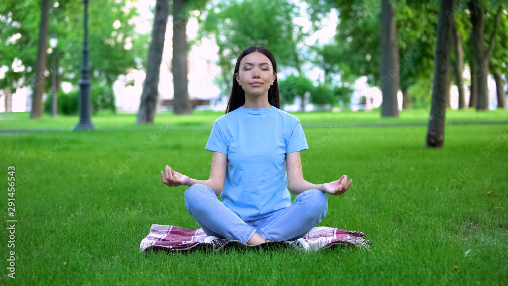 Attractive young lady meditating in park sitting lotus pose, relaxing outdoors Attractive young lady meditating in park sitting lotus pose, relaxing outdoors