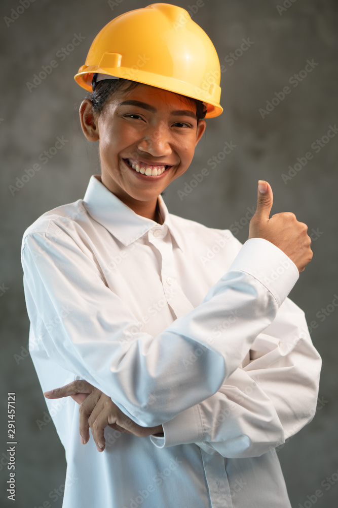 Portrait of smiling Asian woman engineer showing thumbs up gesture over concrete wall background Portrait of smiling Asian woman engineer showing thumbs up gesture over concrete wall background