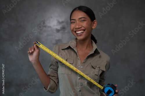 Portrait of smiling Asian woman architect in uniform holding measuring tape over concrete wall. Working concept photo