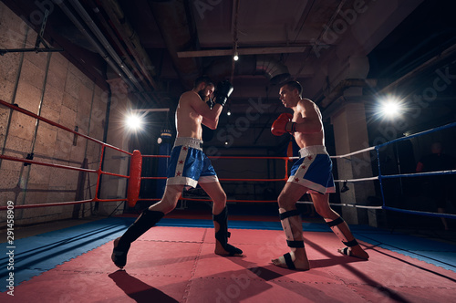 Attractive man fighter exercising kickboxing with sparring partner in the ring at the health club