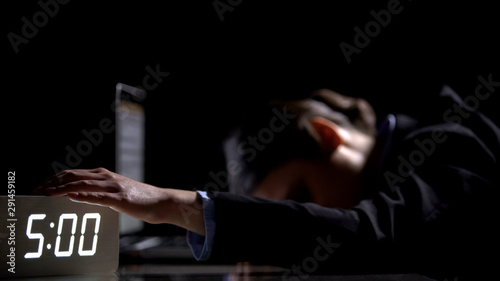 Sleepy lady in suit switching off alarm, lying on laptop in office late at night