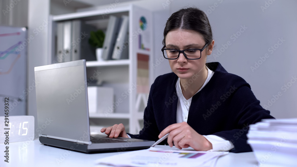 Female office employee looking through information in laptop and documents, work Female office employee looking through information in laptop and documents, work