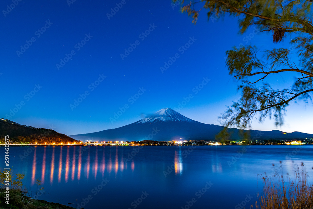 Mount fuji with star in the blue sky and lgiht from the city with tree in forground at Lake kawaguchi in Japan
