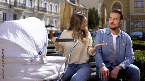 Upset mom worrying about crying baby pram, indifferent husband sitting on bench